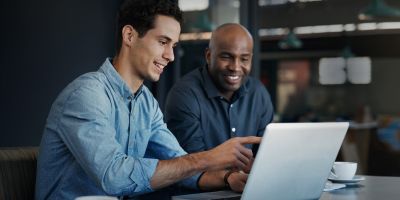 Zwei Menschen sitzen vor einem Laptop und beraten