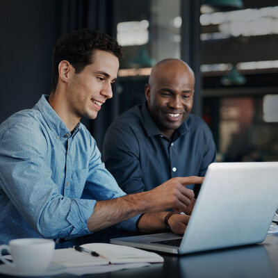 Zwei Menschen sitzen vor einem Laptop und beraten