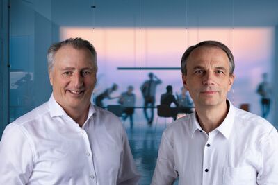 Christoph Machner und Stephan Sequens im Interview Stephan Sequens und Christoph Machner sowie im Hintergrund eine Teambesprechung