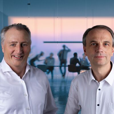 Stephan Sequens und Christoph Machner sowie im Hintergrund eine Teambesprechung